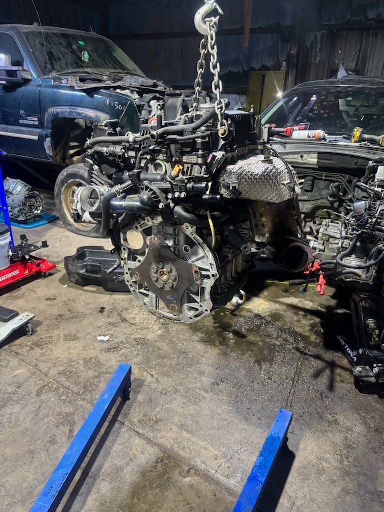 An engine hanging from a hoist chain after being pulled from an SUV